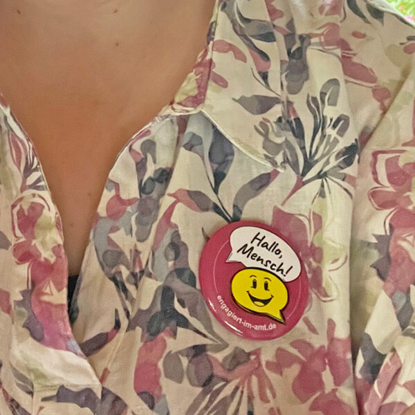 hallo_mensch_kleidung_1080x1080px Ein kleiner Button mit großer Wirkung: „Hallo, Mensch!“ steht für Gesprächsbereitschaft, Gemeinschaft und gelebtes Ehrenamt.